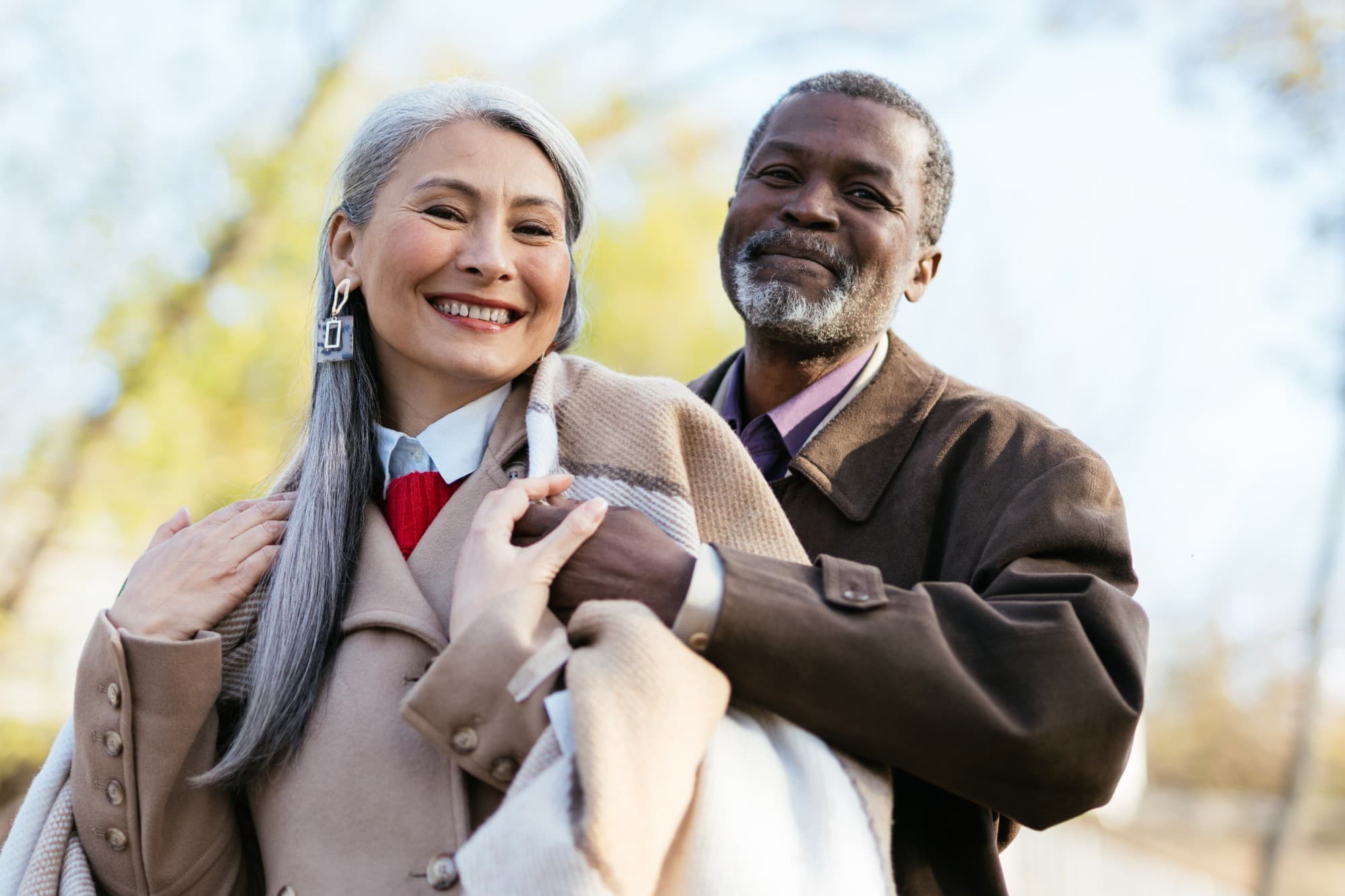 Un couple de personnes âgées souriant, enlacé en extérieur